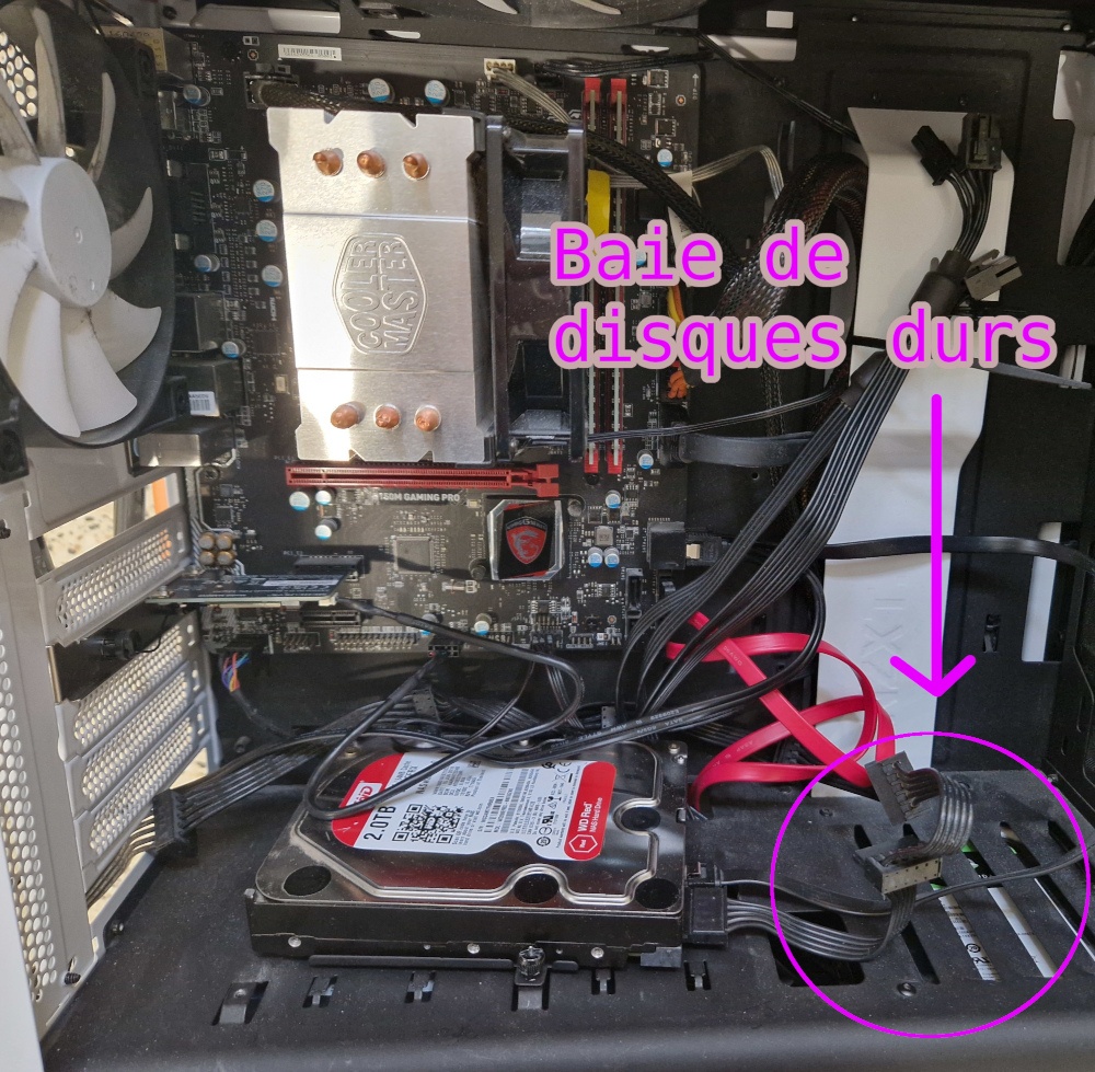 l'intérieur de la tour avec toute la carte mère visible, une flèche vers le bas du chassis couvert d'une tôle en dessous de laquelle sont les disques durs et l'alimentation