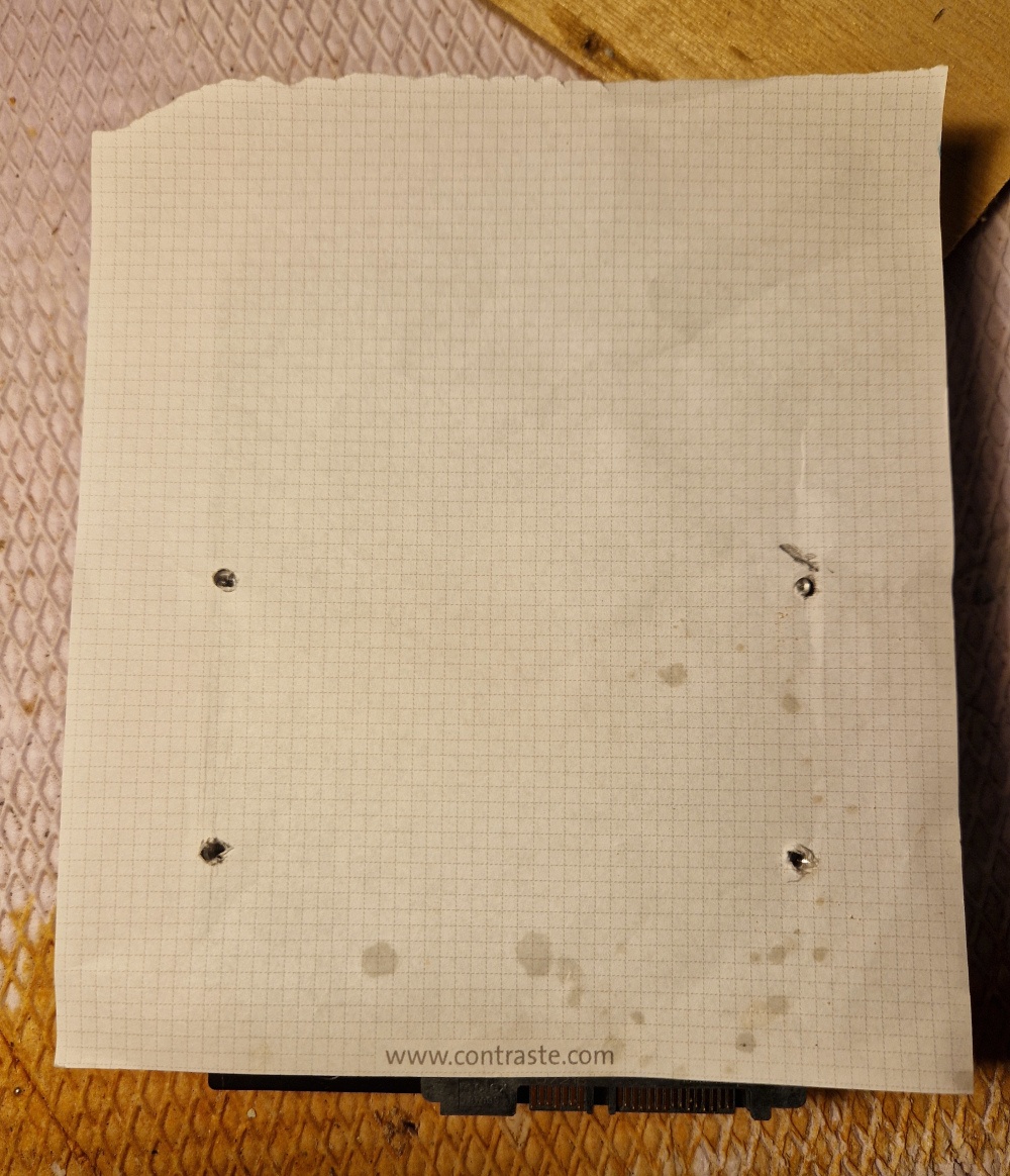 Une petite feuille de papier avec 4 trous qui marquent les emplacemenets des vis sur l'envers du disque dur